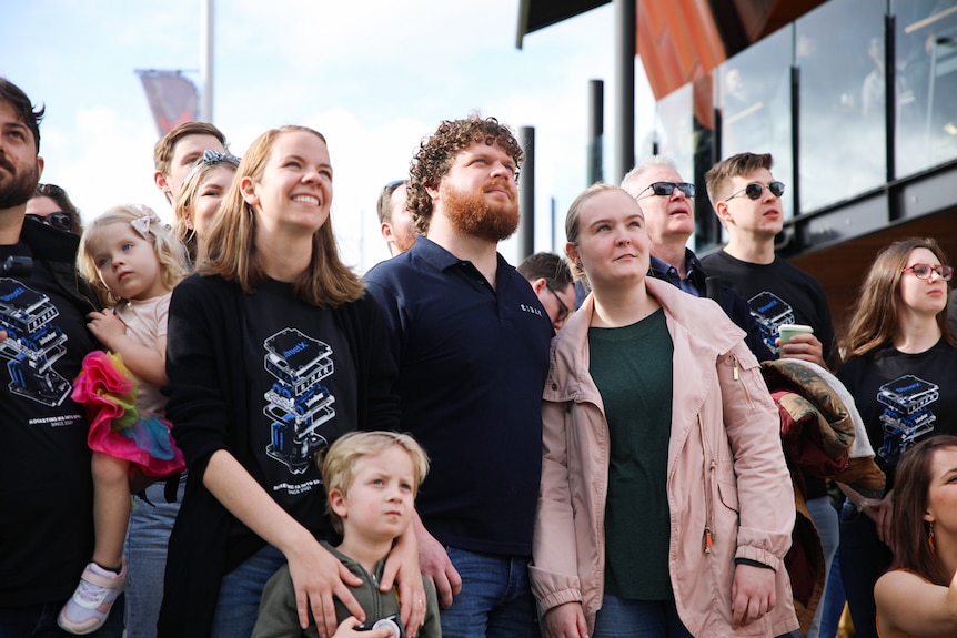 A group of smiling people look up at a screen