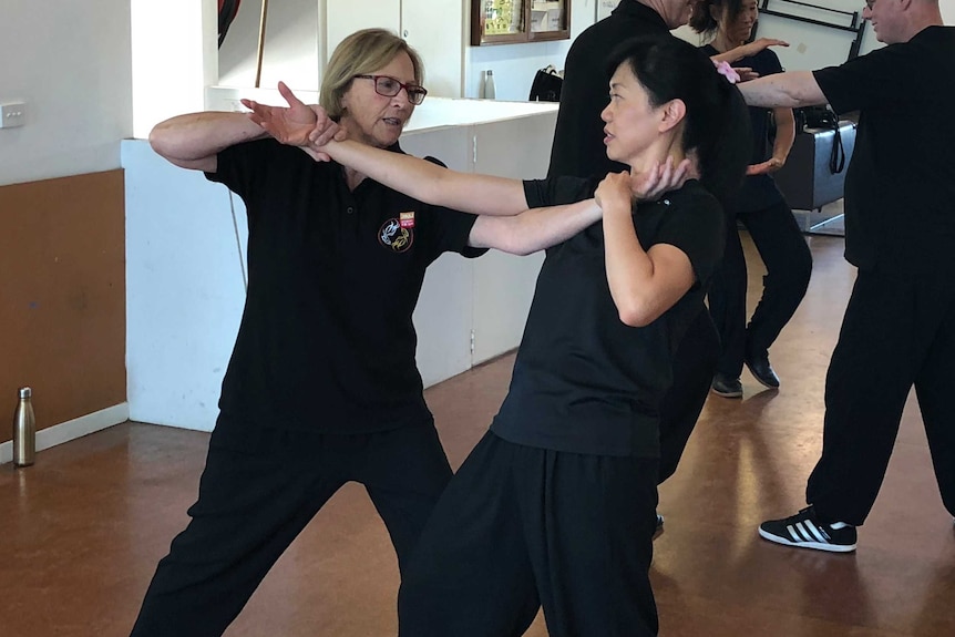 Two women practice Tai Chi in a hall.