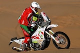 A motorcycle rider stands up on his pedals while riding in sand