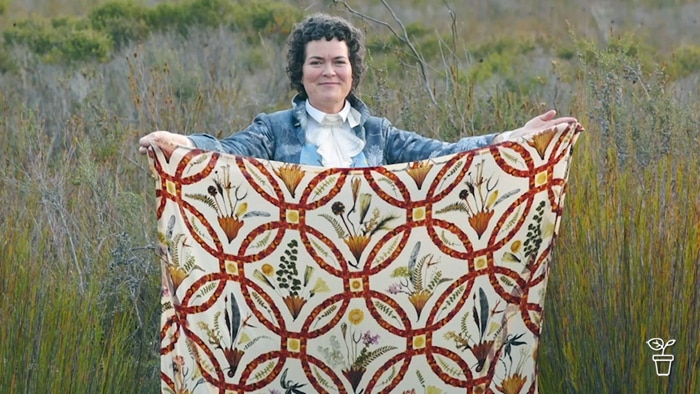 Woman standing in open bushland holding out a piece of fabric decorated with flowers.