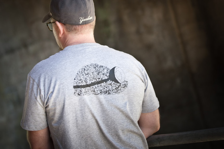 The back view of a man wearing a grey t-shirt and a black cap.