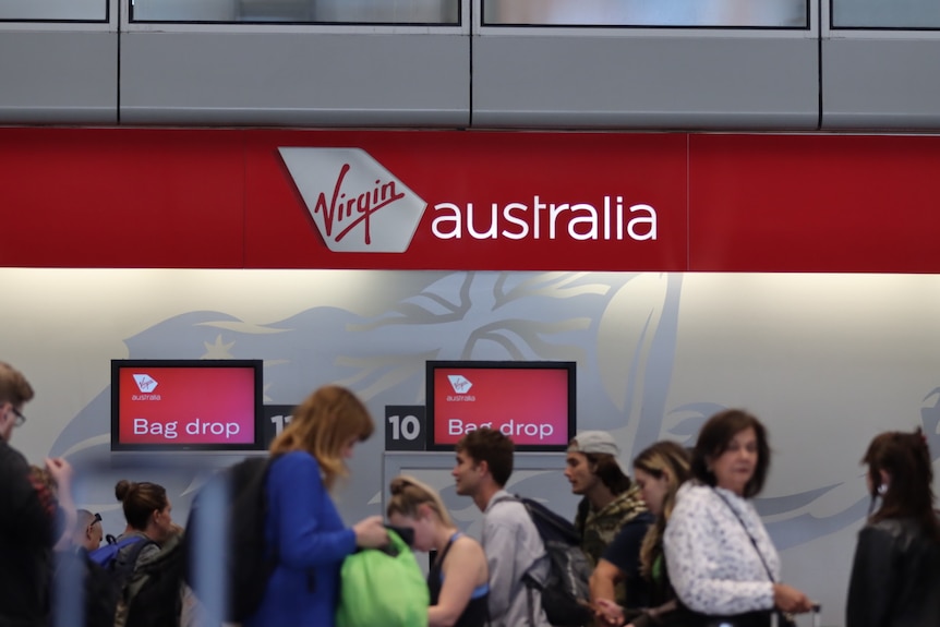 People at Brisbane Airport walk in front of red signs that read 'Virgin Australia bag drop'