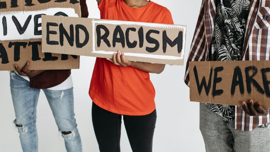 Signs held by three people who's faces are not shown. One signs says 'end racism'.