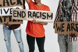 Signs held by three people who's faces are not shown. One signs says 'end racism'.