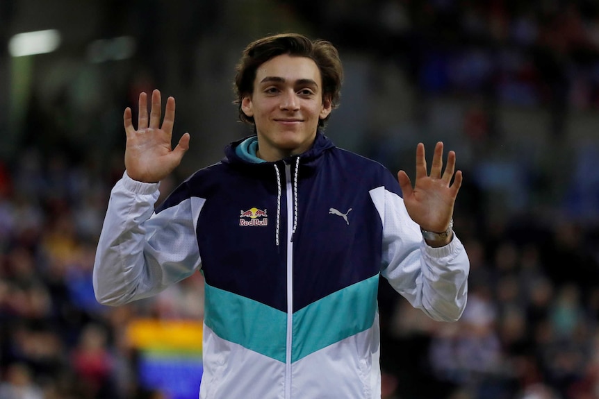 An athlete stands on a podium with raised hands to acknowledge the crowd after his pole vault event.