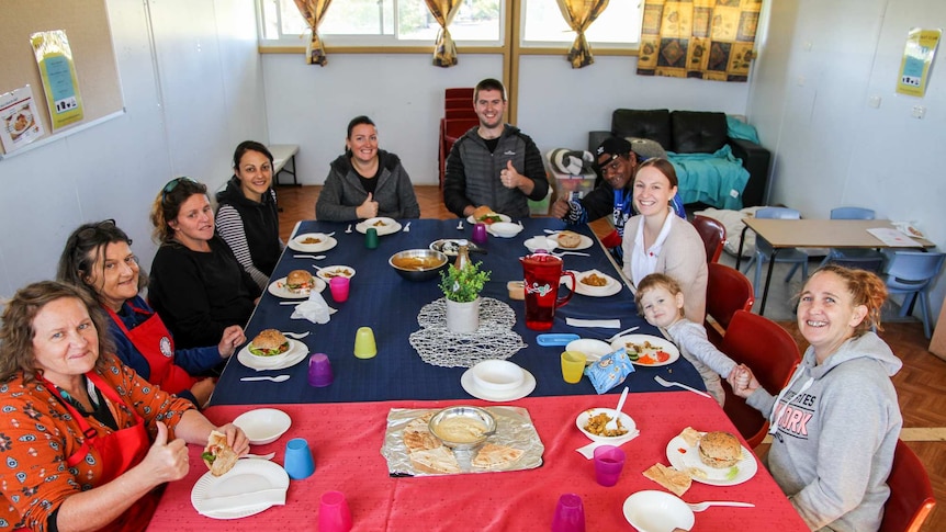 A room full of people sit at a table ready to eat a meal.