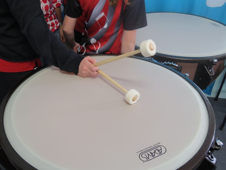 A student holds drumsticks on top of a timpani (a set of drums)