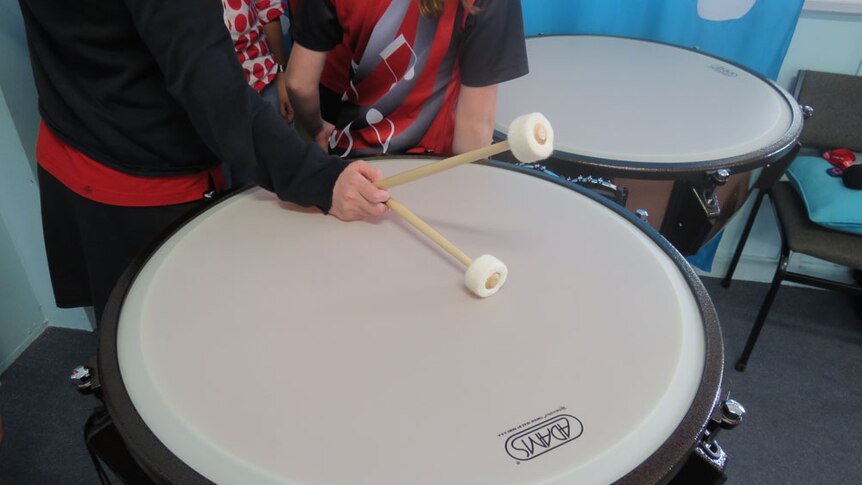 A student holds drumsticks on top of a timpani (a set of drums)