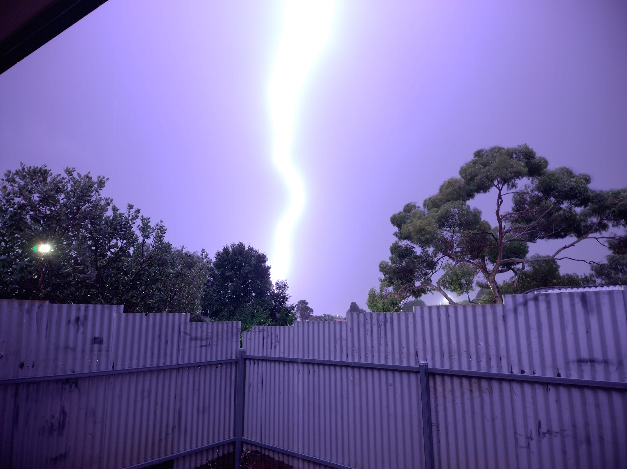 Lighting strike during morning thunderstorm overlooking Morphett Vale in Adelaide, fence at bottom, trees to the side