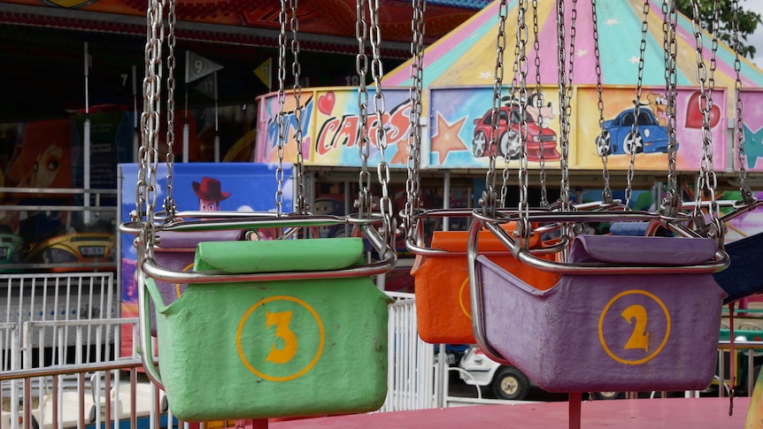 The backs of two empty swing chairs on a carousel.