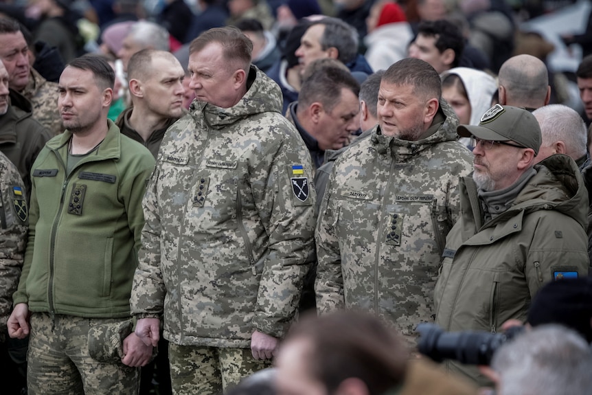 Four men stand in a line in military greens. 