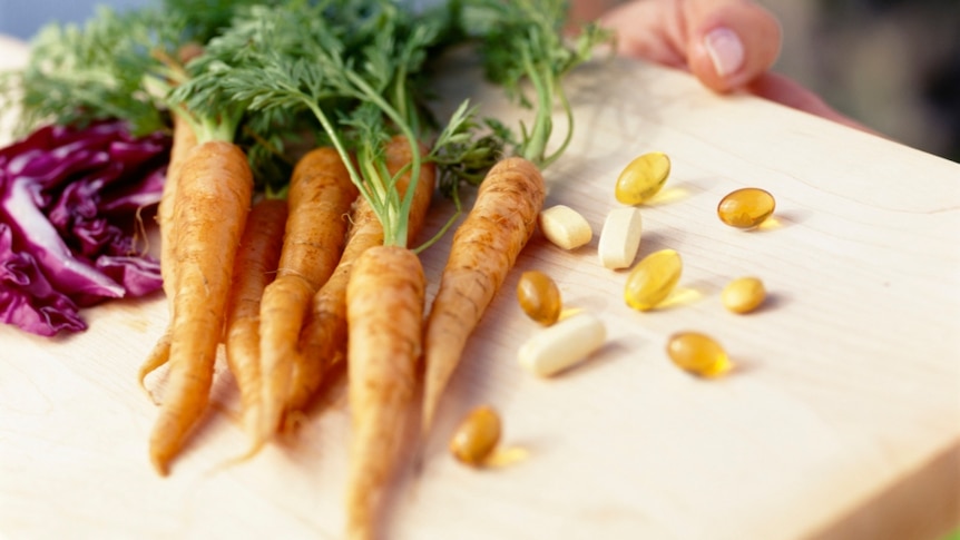 Carrots and vitamin supplements on a wooden chopping board