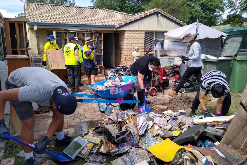 An army of volunteers clear up rubbish at the front of a home in Booval.