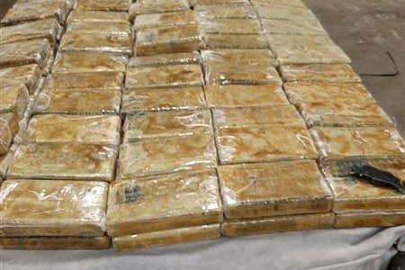 A long line of small packets of cocaine in plastic is displayed on a warehouse floor.