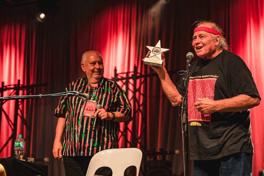 Kev Carmody holds a star shaped trophy aloft as festival director Peter Noble looks on