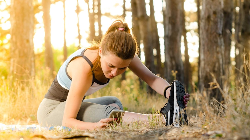 A woman wearing workout clothing and stretching in the woods.