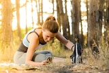 A woman wearing workout clothing and stretching in the woods.