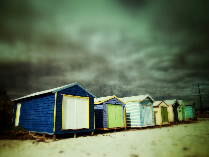 Storm clouds massing behind bayside bathing boxes in Melbourne