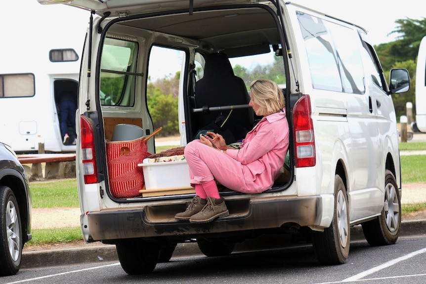 A woman checks her phone while sitting in the back of a van.