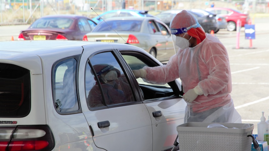 A health worker in head to toe PPE swapping a driver at a COVID testing clinic