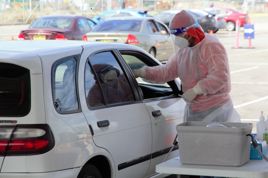 A health worker in head to toe PPE swabbing a driver at a COVID testing clinic.