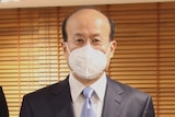 Five men wearing masks and suits pose for a photo inside an office.