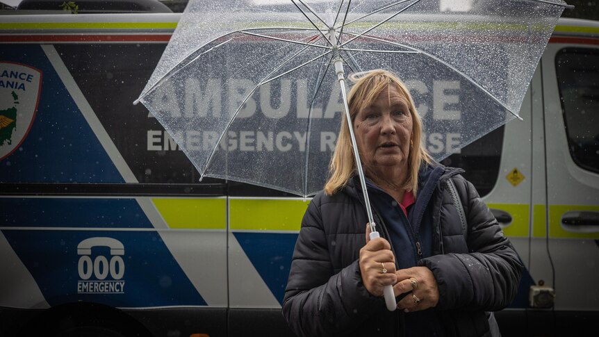 A hospital cleaner stands with an umbrella in front of an ambulance 