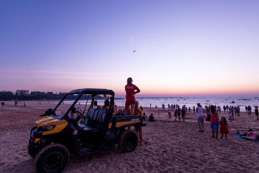 A lifeguard standing on the back of a buggy watches a firework go off on Mindil Beach, at sunset.