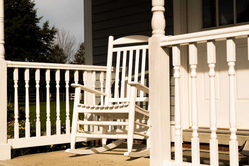 A white wooden rocking chair sits on a wooden porch.