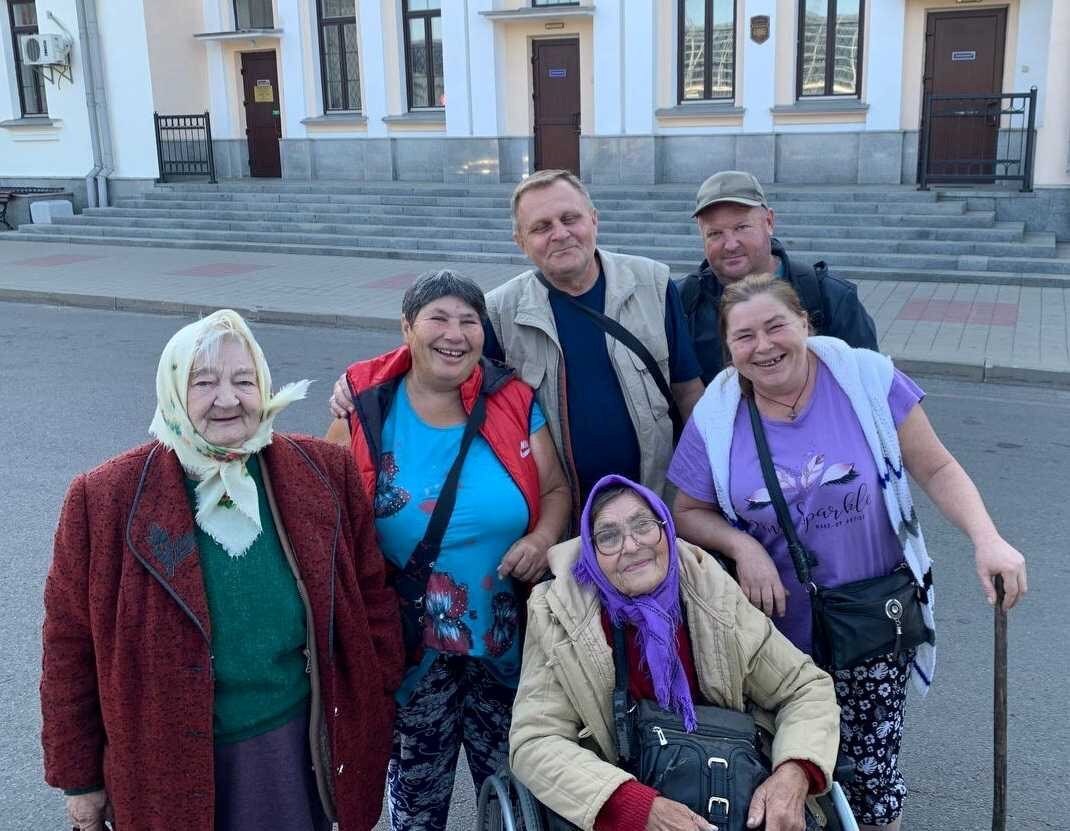 A group of older Ukrainians in a group smile for a photos in an outdoor location. 