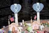 Two blue hearts with writing are placed at a memorial along with candles and flowers.