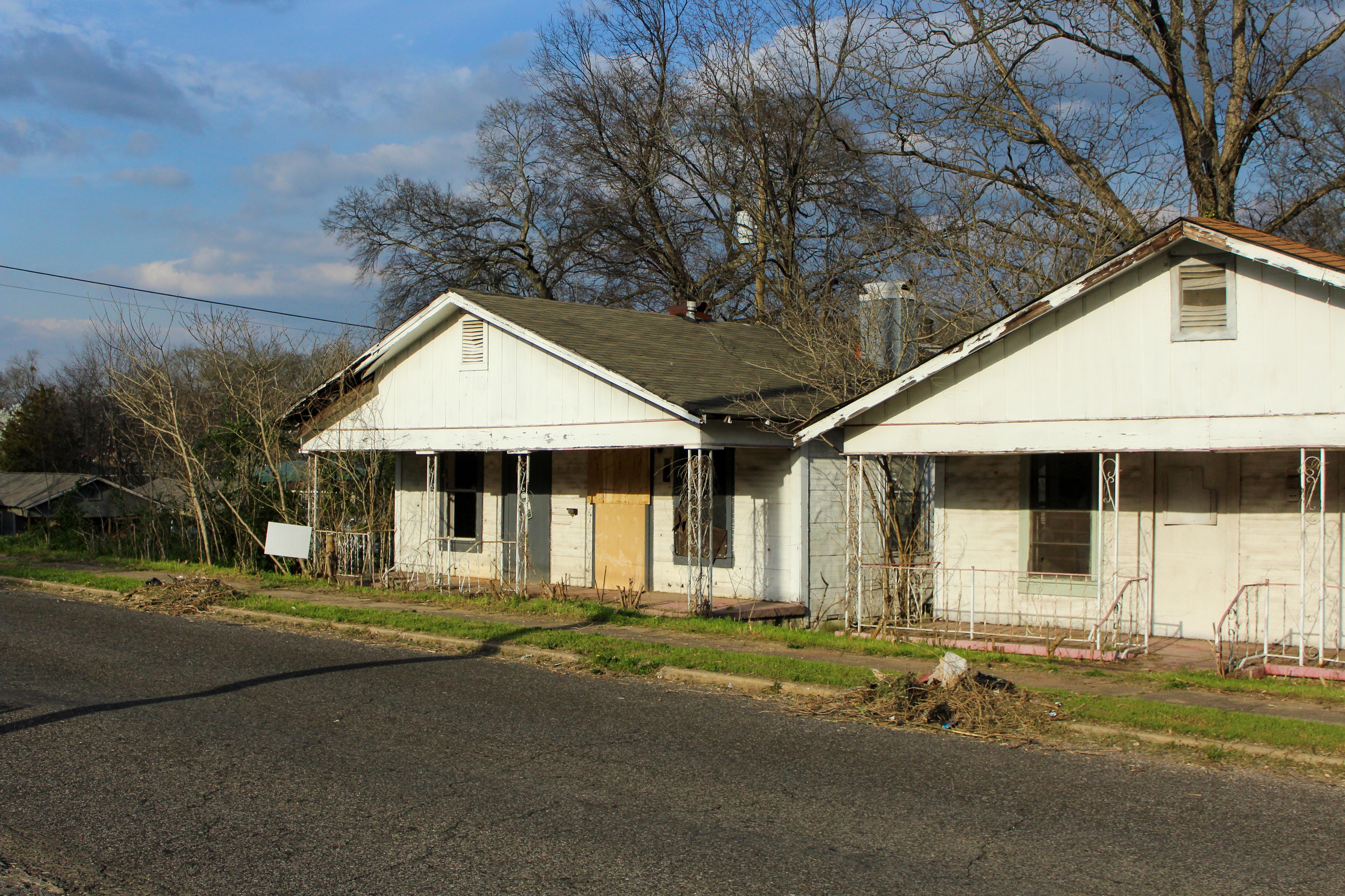 Two boarded up and dilapidated houses sit on an empty street.