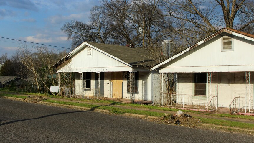 Two boarded up and dilapidated houses sit on an empty street.