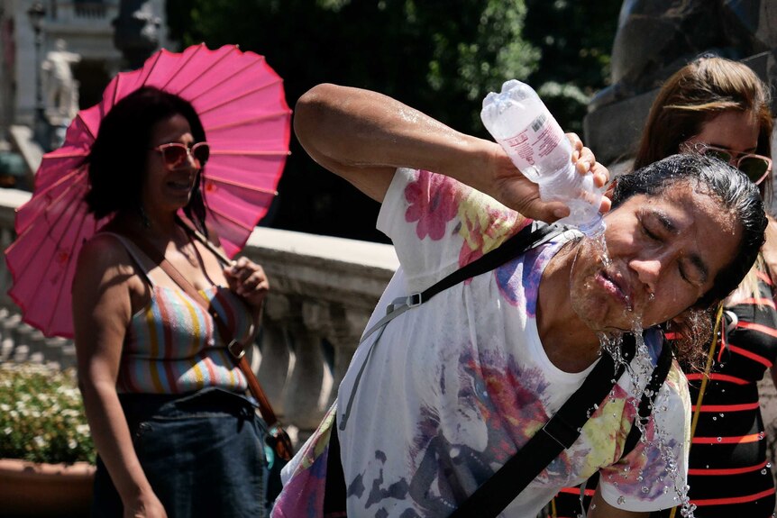 A tourists refreshes by pouring a bottle of water over her face.