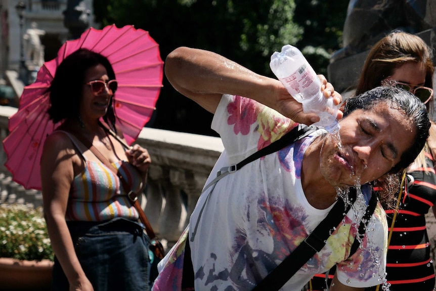 A tourists refreshes by pouring a bottle of water over her face.