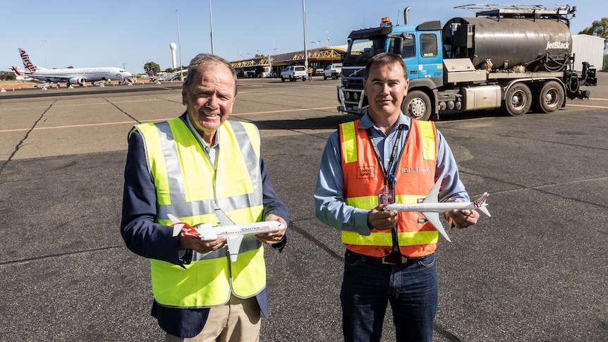 Two men in high-vis workwear holding miniature model aeroplane on the tarmac at an airport.  