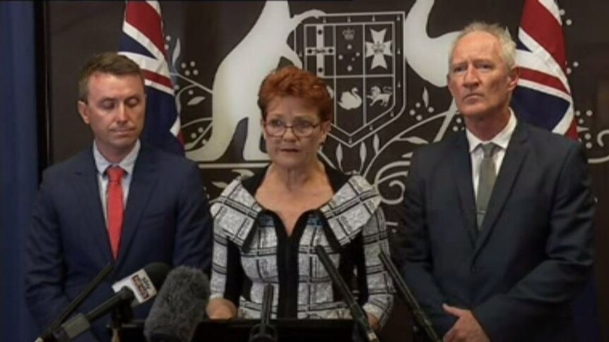 The three people front a media conference with Australian flags and an emblem behind them