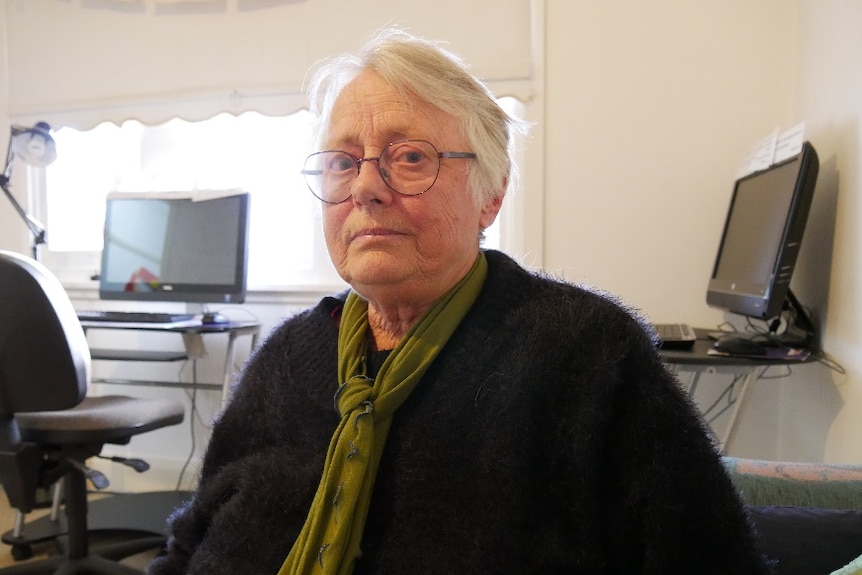 Wendy sits wearing a black fluffy jumper, green scarf and glasses.