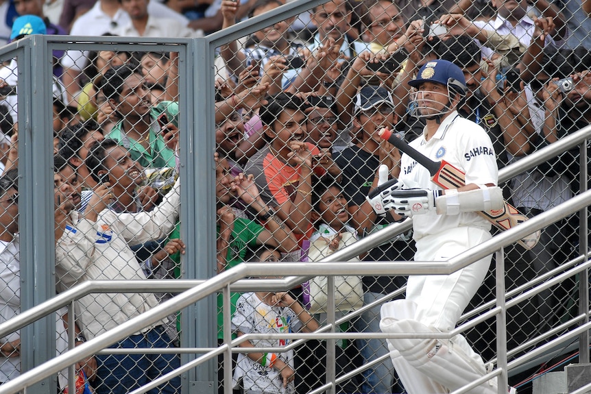 A cricketer walks onto the field as fans clamber to get a glimpse.