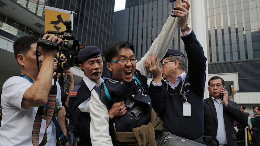 Security guards hold a protestor in front of an office building.