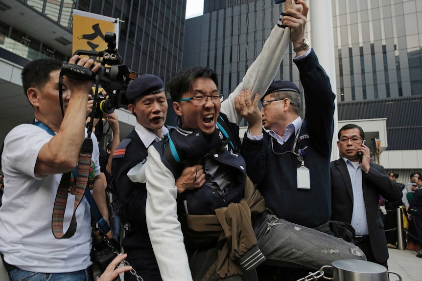 Security guards hold a protestor in front of an office building.