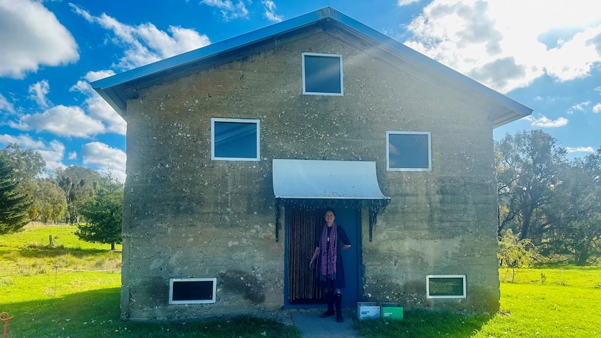 Renovated rock shed in the middle of a paddock with woman standing in open doorway