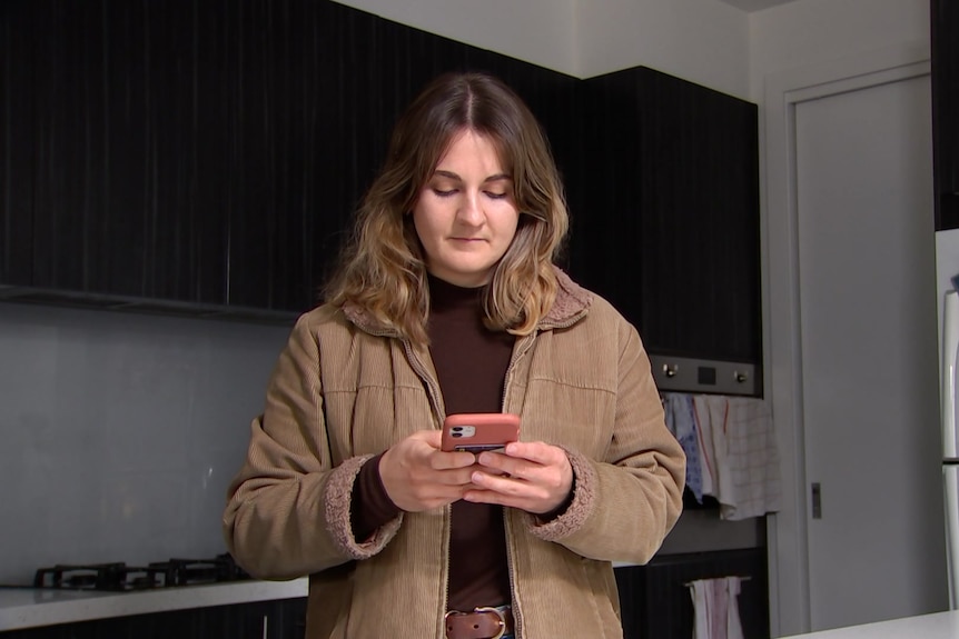 a woman with light brown hair using her phone in a kitchen.