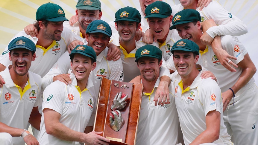 The Australian players crowd around the trophy while smiling and celebrating.