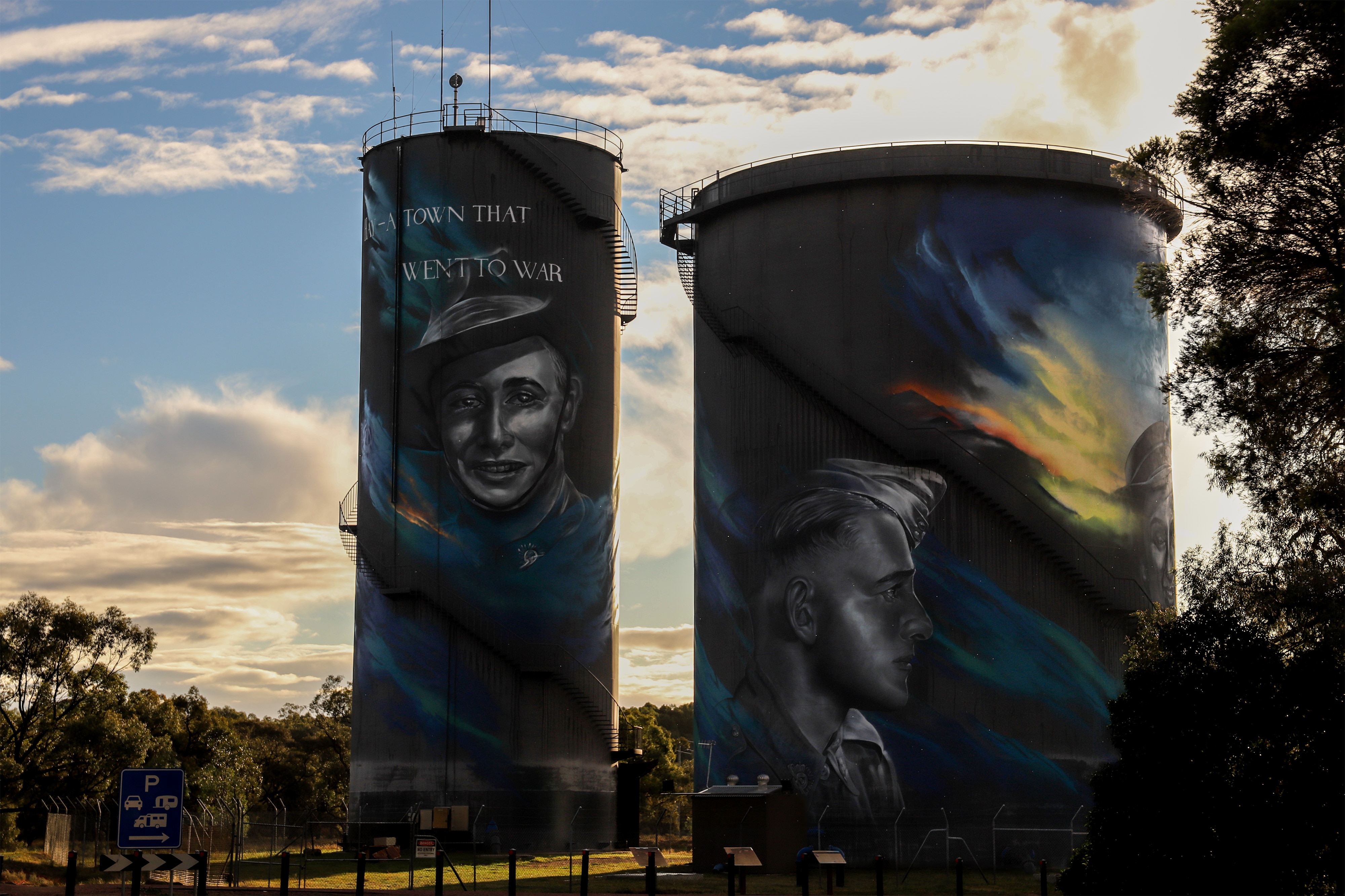 Two large concrete water towers with colourful artwork of soldiers and text beneath an afternoon skyline