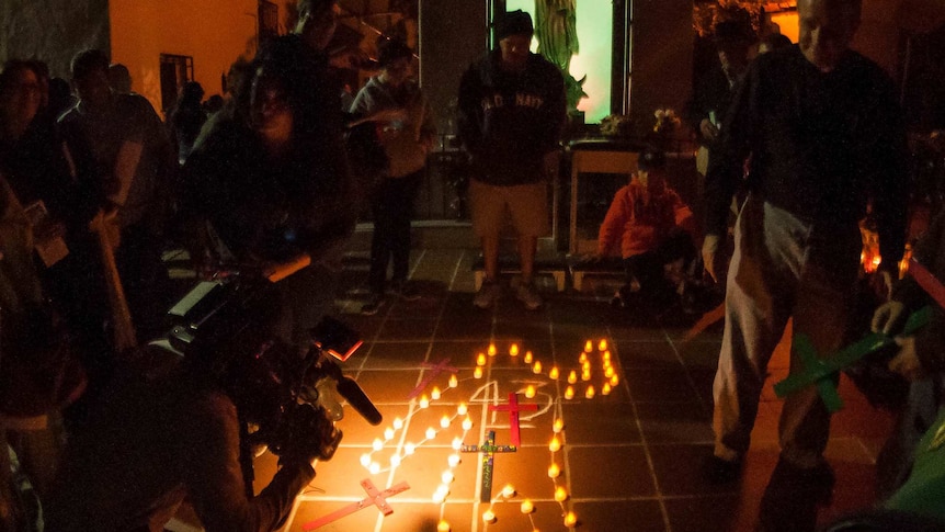 A group gathers at night around an outline of a body on the ground, illuminated by candles for the missing 43 Mexican students.