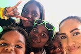 Tahnee Jash and four Indigenous children smiling and making hand signals at camera.
