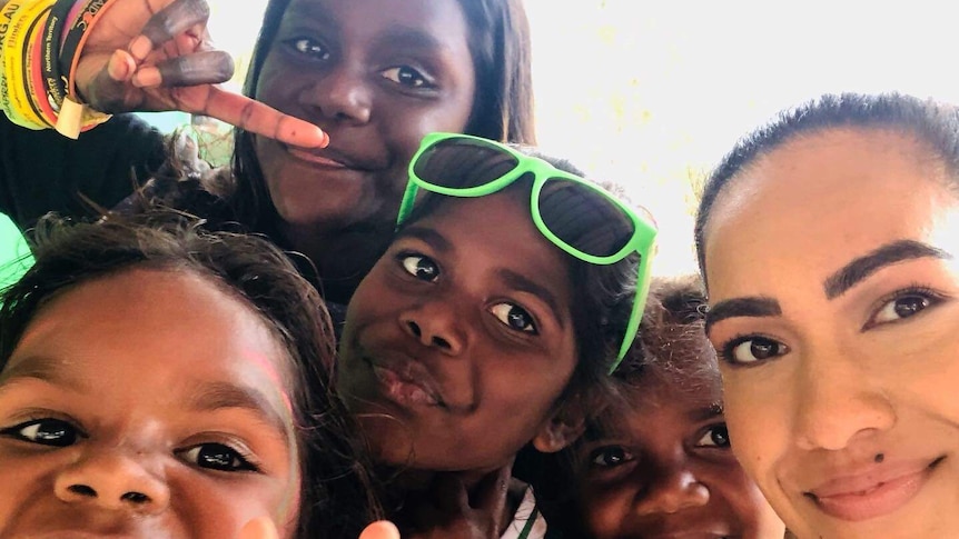 Tahnee Jash and four Indigenous children smiling and making hand signals at camera.