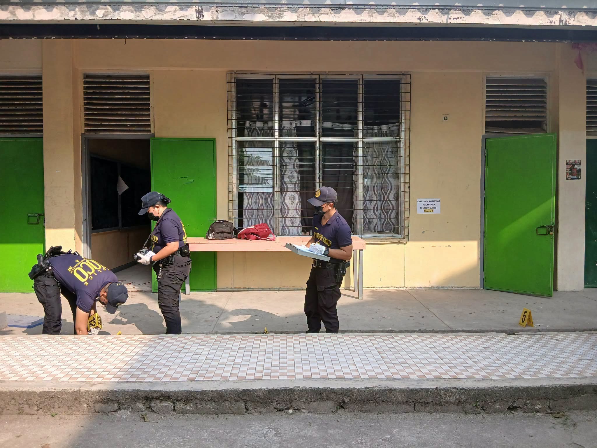 Three Filipino police officers examine scene outside a classroom where a shooting occurred.