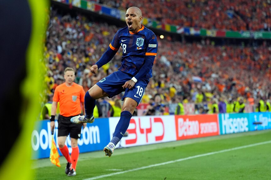 A Dutch footballer leaps in the air near the corner flag in celebration after scoring a goal.